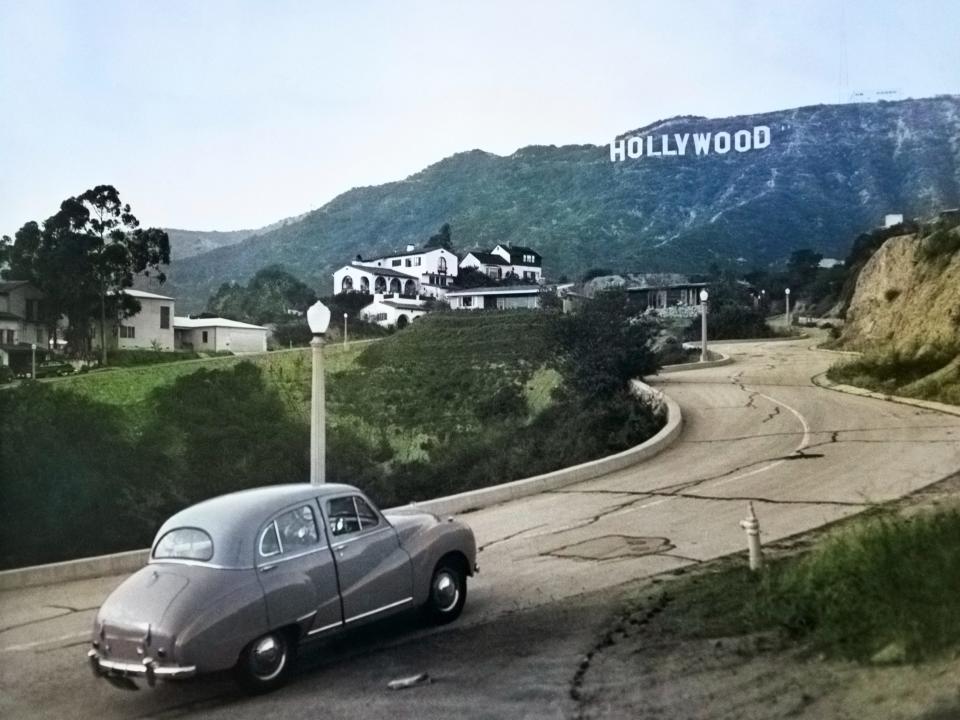 A 1950s Austin car driving up a road in the Hollywood Hills with the Hollywood Sign in the distance in Los Angeles, California.