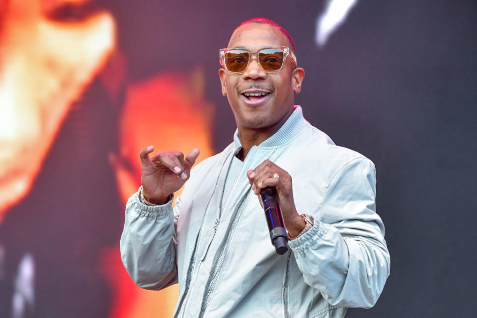 Ja Rule on stage performing, wearing a light jacket and sunglasses, with a microphone in hand