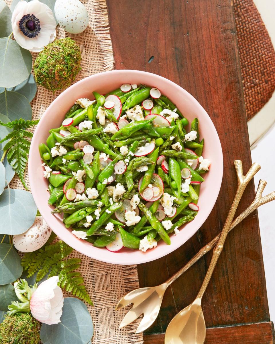 asparagus snap pea and radish salad in a large light pink serving bowl with gold serving utensils