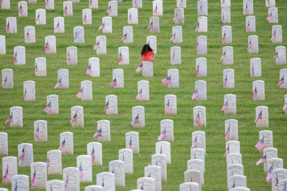 A young girl tries to fit her shirt over the top of a headstone on Memorial Day at the Los Angeles National Cemetery.