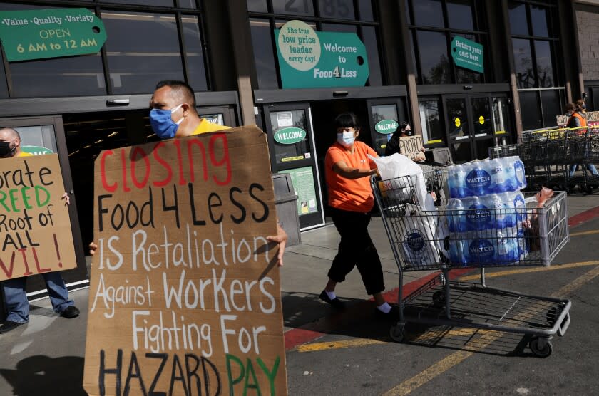 LONG BEACH-CA-3 FÉVRIER 2021: Un acheteur passe devant un groupe tenant des pancartes en faveur de Food 4 Less workers à l'épicerie de South Street à North Long Beach le mercredi 3 février 2021. Food 4 Less workers, city Les dirigeants et les défenseurs des travailleurs locaux tiennent une conférence de presse pour appeler Kroger Co., la société mère de Food 4 Less et Ralph's, à maintenir les magasins ouverts et à condamner les actions de l'entreprise visant à fermer deux de ses sites à la ville en raison de l'ordonnance d'urgence de la ville pour 4 $ de l'heure en prime de risque temporaire.  (Christina House / Los Angeles Times)