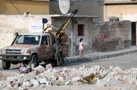 A girl walks near a truck mounted with a weapon in the border town of Tal Abyad