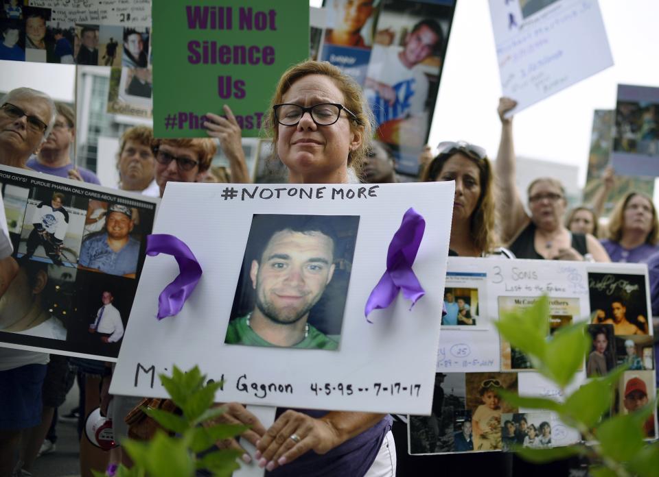 FILE - In this Friday, Aug. 17, 2018, file photo, Christine Gagnon of Southington, Conn., protests with other family and friends who have lost loved ones to OxyContin and opioid overdoses at Purdue Pharma LLP headquarters in Stamford, Conn. Gagnon lost her son Michael 13 months earlier. Reports emerging about a possible financial settlement in 2019 with Purdue Pharma, the company that has come to symbolize the nation's opioid epidemic, suggests the settlement amount won't come anywhere near what the national crisis has cost. (AP Photo/Jessica Hill, File)