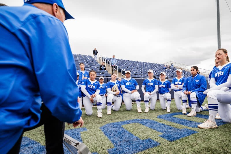 Under gray skies, members of the BYU softball team take a knee to listen to their coach prior to game against Oklahoma State on March 23 in Provo. Gray skies and inclement weather are what players sign up for when playing spring sports in Utah. | Aaron Cornia/BYU