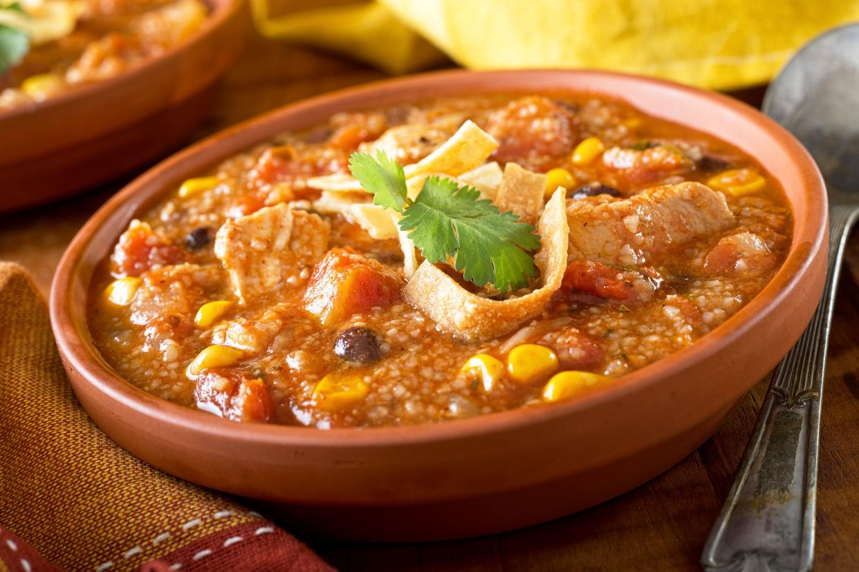 Closeup of slow-cooker chicken-tortilla soup in a earthenware terracotta bowl with a spoon and napkin with a blurred background