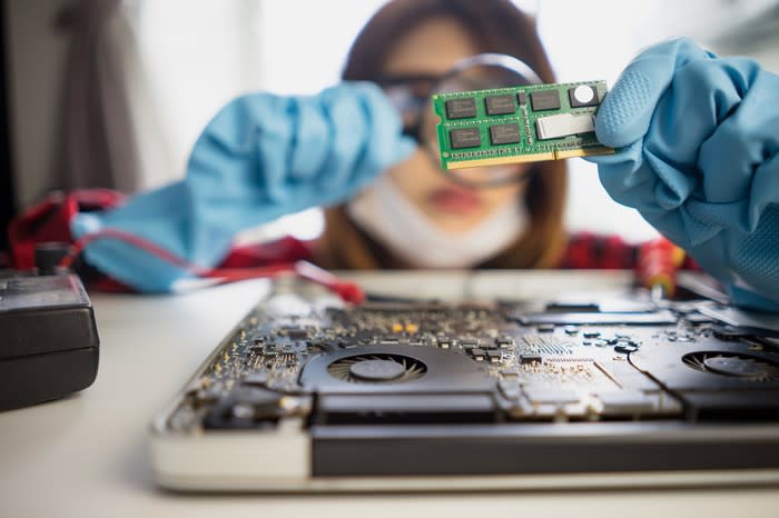 An Asian female worker with blue gloves inspects a memory card with a magnifying glass.