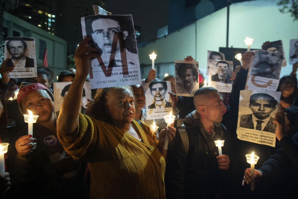 In this Aug.5, 2019 file photo, demonstrators hold photos of people killed during Brazil's dictatorship outside a police station that used to be a torture center used by the dictatorship, as they protest President Jair Bolsonaro's removal of members of a commission investigating disappearances and murders that took place during Brazil's dictatorship in Sao Paulo, Brazil. Carlos Bolsonaro, one of the sons and political aids of Brazilian President Jair Bolsonaro, has caused an uproar saying democracy is slowing development in Latin America's biggest country. (AP Photo/Andre Penner, File)
