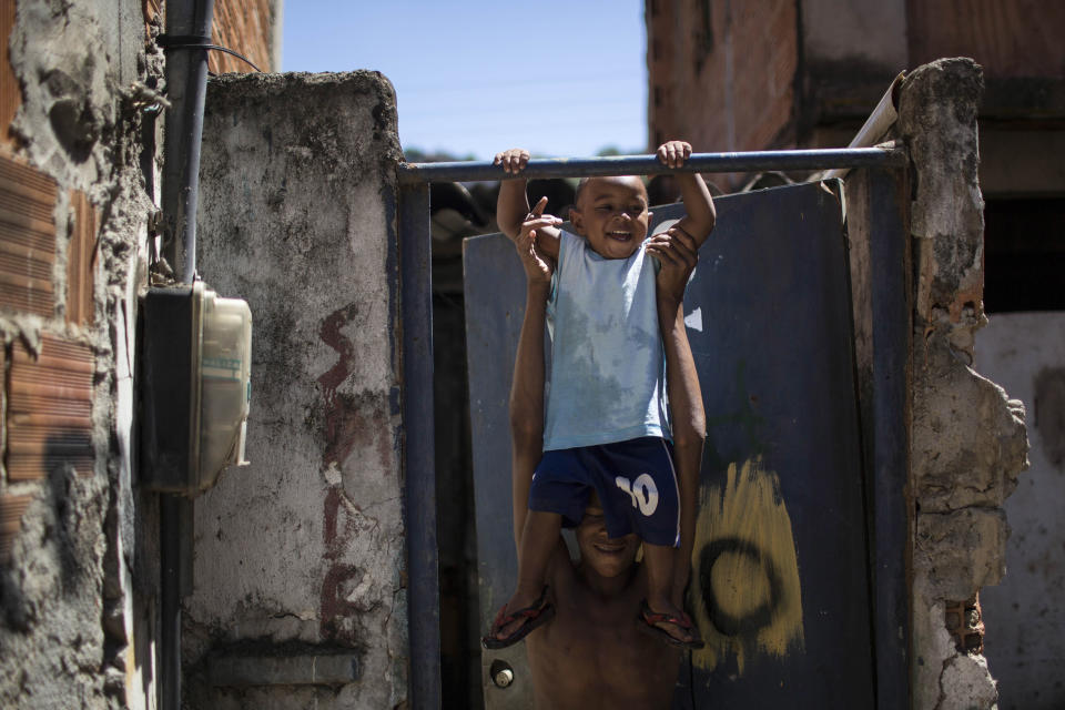In this Jan. 10, 2014 photo, a man plays with a toddler inside the Favela do Metro slum in Rio de Janeiro, Brazil. Some residents in this slum were evicted from their homes two years ago for the area to be renovated for this year's World Cup and 2016 Olympics, but people reoccupied the homes and are fighting to stay. (AP Photo/Felipe Dana)