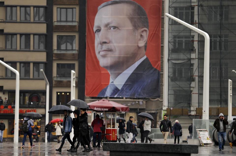 In this Tuesday, March 14, 2017 photo, people walk in central Istanbul's Taksim Square, backdropped by a poster of Turkish President Recep Tayyip Erdogan. The entire Turkish referendum campaign has been biased and unfair, those opposed to expanding the president’s powers say, noting they have been hampered by a lack of TV airtime, threats, violence, arbitrary detentions and even sabotage. Those reports come even as Erdogan himself has slammed European countries for not letting his ministers campaign on their soil for the April 16 vote on expanding his powers. (AP Photo/Lefteris Pitarakis)