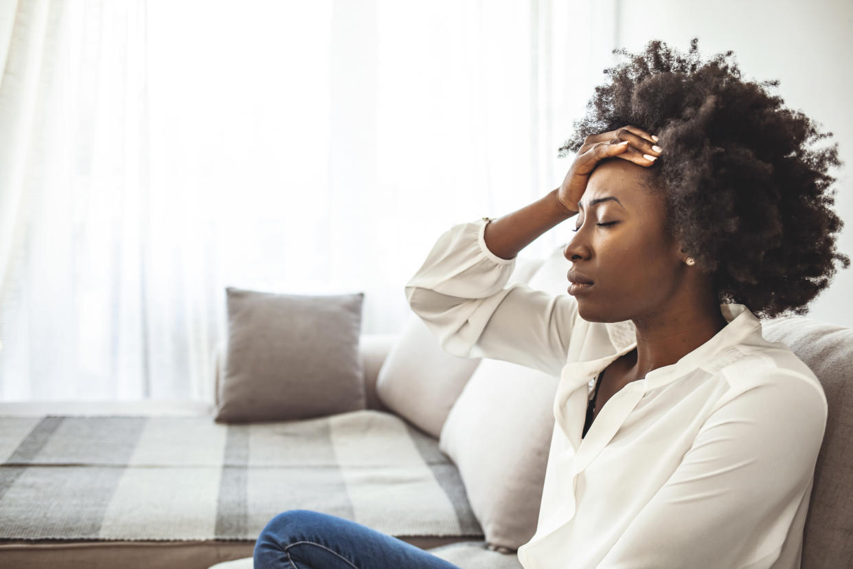 Lonely sad woman deep in thoughts sitting daydreaming or waiting for someone in the living room with a serious expression, she is pensive and suffering from insomnia sitting on couch