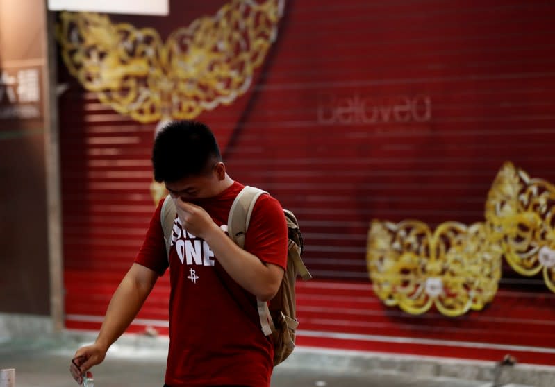 A pedestrian covers his face with his T-shirts from the tear gas as he walks past a jewelry shop during an anti-government protest in Hong Kong