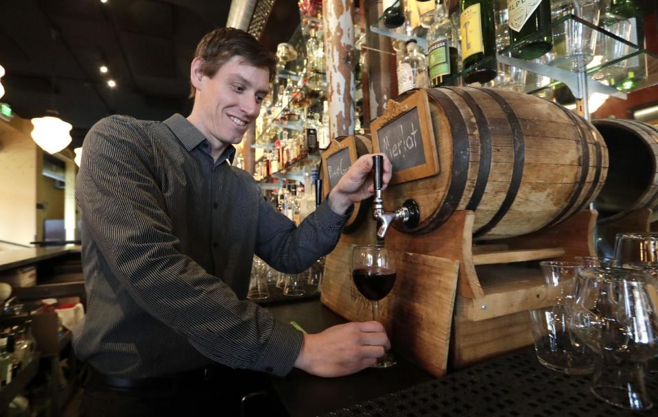 In this photo taken Tuesday, Jan. 10, 2017, restaurant manager Jason Appleton pours a glass of wine from a small barrel at Luc's restaurant as he demonstrates that the same system could be used for consumers using their own growlers, in Seattle. Wine drinkers are one step closer to being able to purchase and refill their favorite pours in reusable growlers closer to home instead of making a trip to the winery. Some state winemakers are pushing House Bill 1039 as a way to expand wine sales and reduce the carbon footprint of wine bottles. If approved, consumers would be able to bring or buy refillable growlers at any business that has the license to sell wine. (AP Photo/Elaine Thompson)
