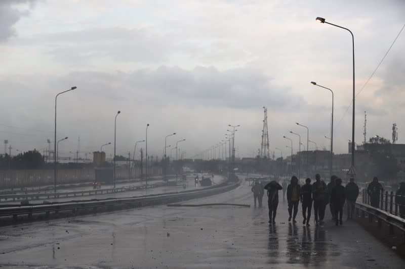 Iraqi demonstrators walk as they block the highway during ongoing anti-government protests in Baghdad