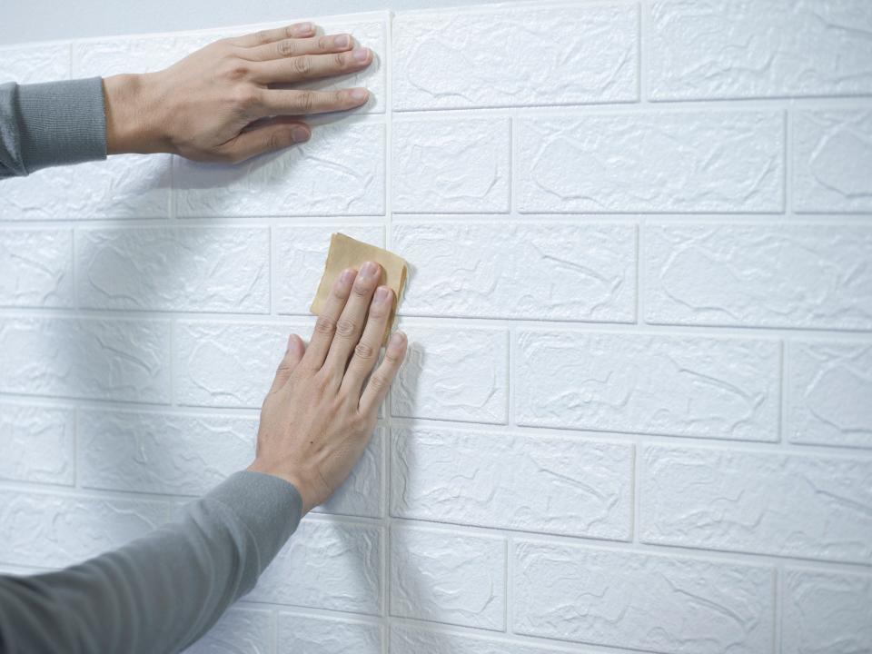 Person smoothing out white subway tile contact paper on kitchen backsplash