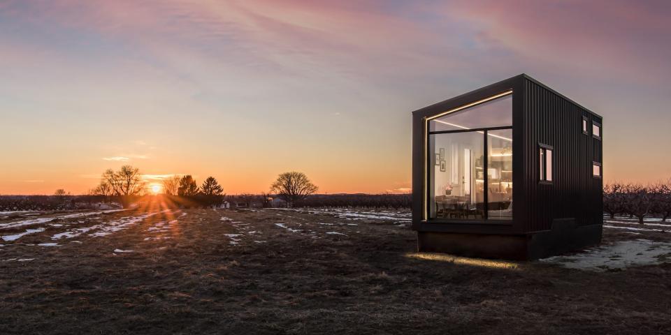 a black tiny home with a large glass wall on a snowy field