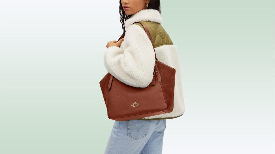 Model wearing the brown leather and suede tote bag on their shoulder on a green background. 