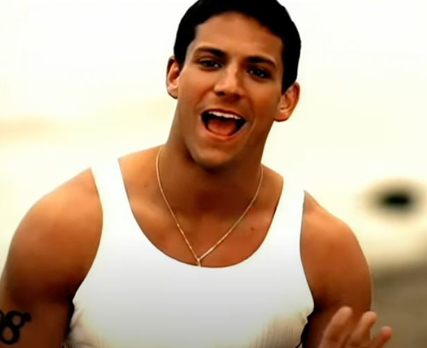 Man in a white tank top singing with an open mouth