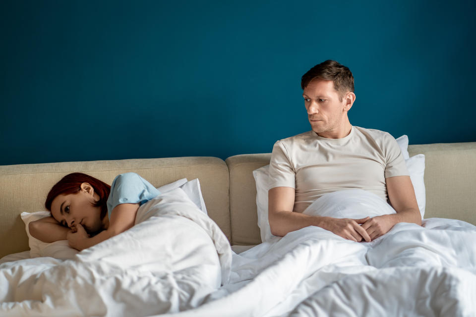 Two individuals in bed; one asleep and the other awake and contemplative