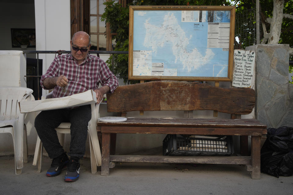 An elderly resident tends to a patch of herbs outside his store on the Aegean Sea island of Tilos, southeastern Greece, Tuesday, May 10, 2022. When deciding where to test green tech, Greek policymakers picked the remotest point on the map, tiny Tilos. Providing electricity and basic services, and even access by ferry is all a challenge for this island of just 500 year-round inhabitants. It's latest mission: Dealing with plastic. (AP Photo/Thanassis Stavrakis)