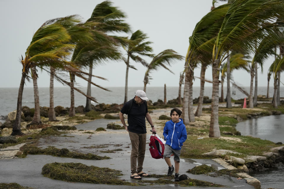 Bob Givehchi, left, and his son Daniel, 8, Toronto residents visiting Miami for the first time, walk past debris and palm trees blowing in gusty winds, at Matheson Hammock Park in Coral Gables, Fla., Friday, Dec. 15, 2023. It's beginning to look at lot like…hurricane season, at least across much of South Florida, where it's been windy and rainy for two days and the forecast predicts more of the same this busy holiday season weekend. (AP Photo/Rebecca Blackwell)