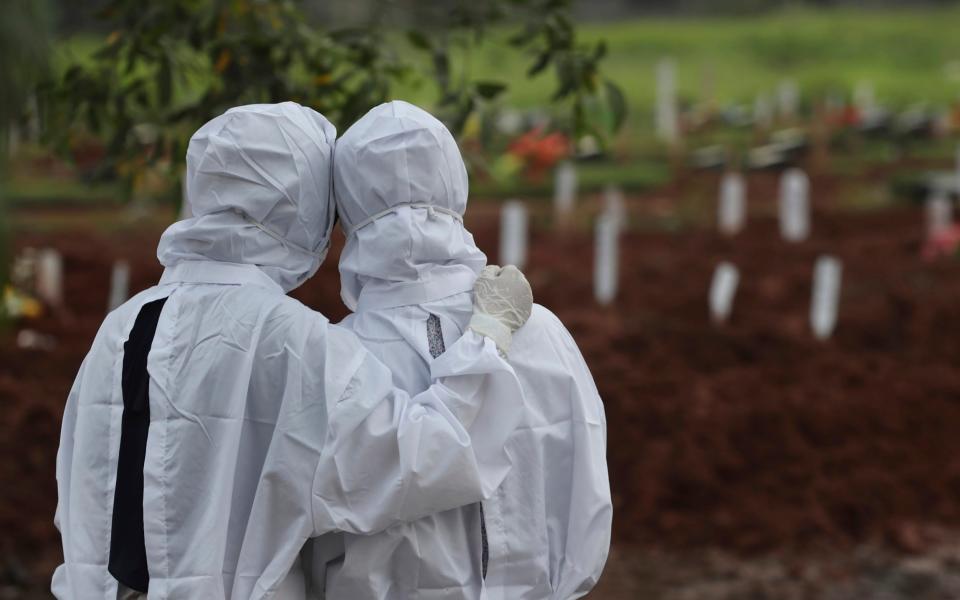 Family members watch workers bury a coffin at a special Covid cemetery in Bekasi, West Java, Indonesia - Achmad Ibrahim/AP