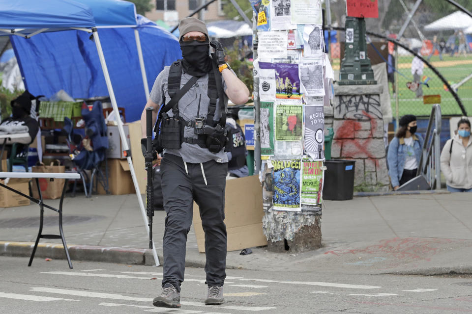 A member of the volunteer security team at the Capitol Hill Occupied Protest Zone carries a rifle as he walks Saturday, June 20, 2020, inside the CHOP in Seattle. Armed volunteers said they were patrolling Saturday to keep the area safe. A pre-dawn shooting Saturday near the area left one person dead and critically injured another person, authorities said Saturday. The area has been occupied by protesters after Seattle Police pulled back from several blocks of the city's Capitol Hill neighborhood near the Police Department's East Precinct building. (AP Photo/Ted S. Warren)