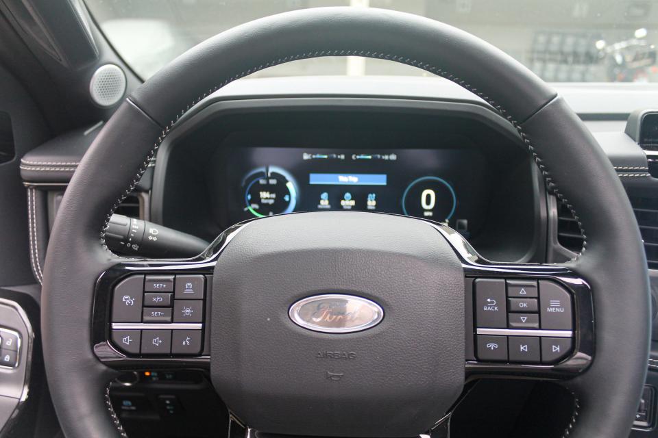 The steering wheel of the 2023 Ford F-150 Lightning Platinum, with a screen behind displaying speed and other data.