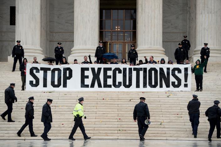 Fourteen police officers surround a row of anti-death penalty activists holding a banner saying Stop Executions!, on the steps of the Supreme Court.