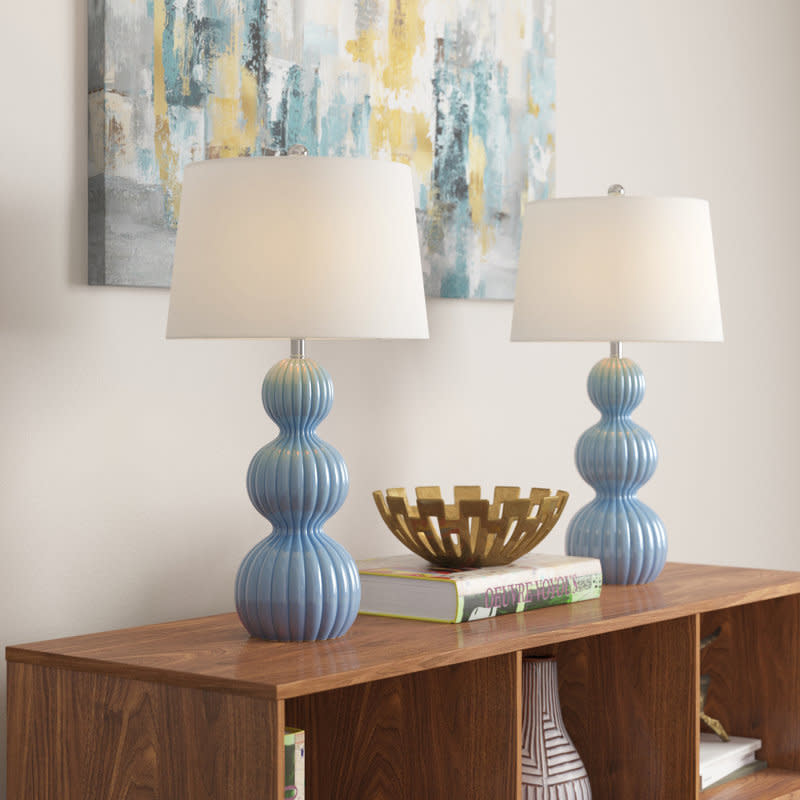 Two blue ceramic table lamps with white shades on a wooden console, next to a decorative gold bowl and books