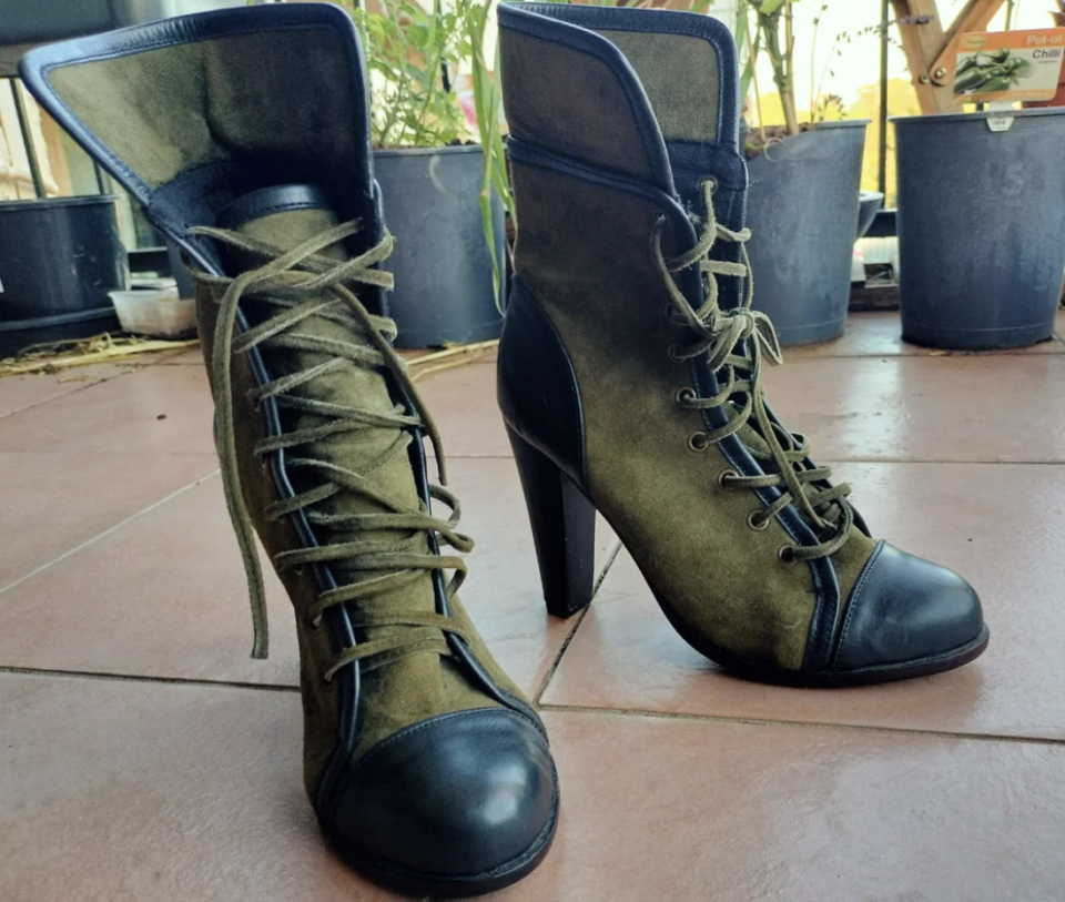 A pair of lace-up heeled ankle boots on a tiled surface, with plant pots in the background