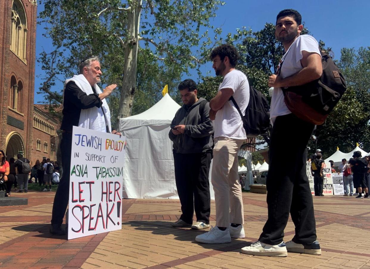 A professor holds a sign reading "Let Her Speak!"