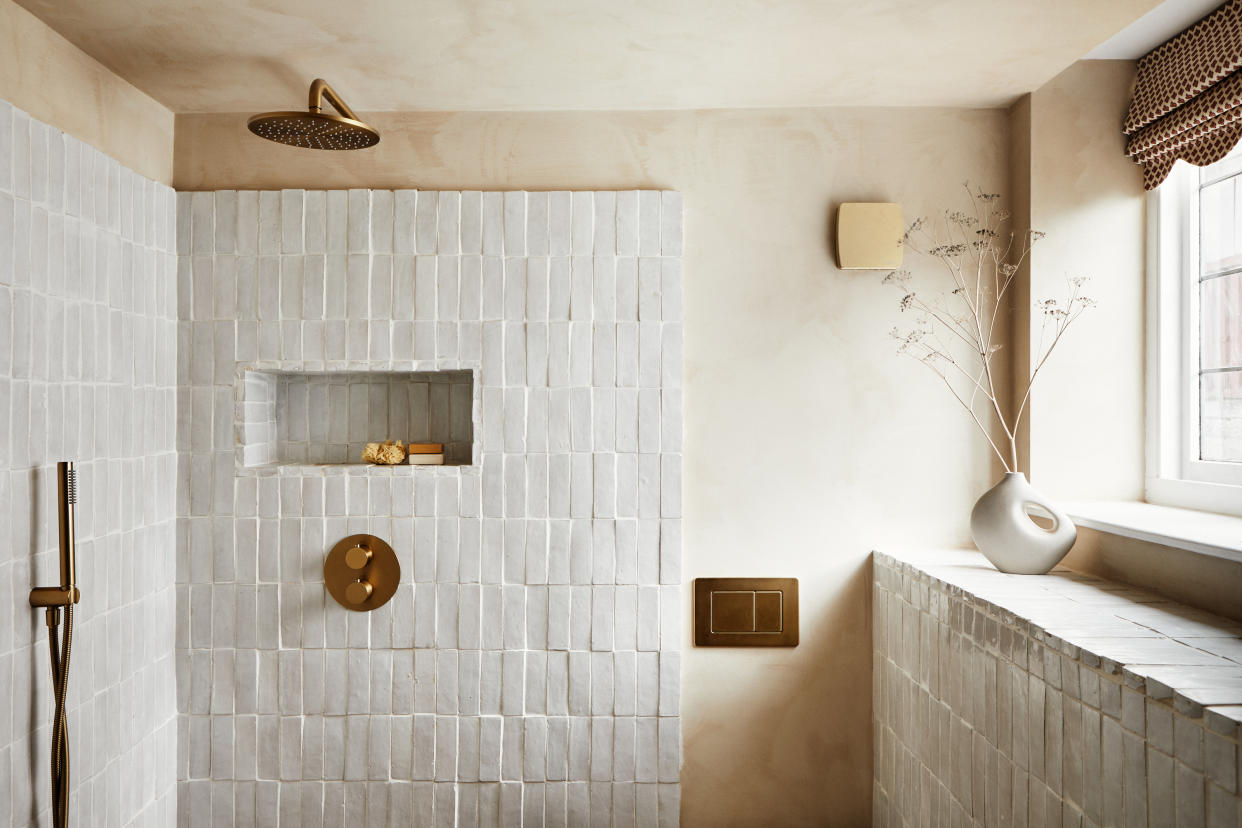  A bathroom with white zellige tiles and gold plumbing fixtures 