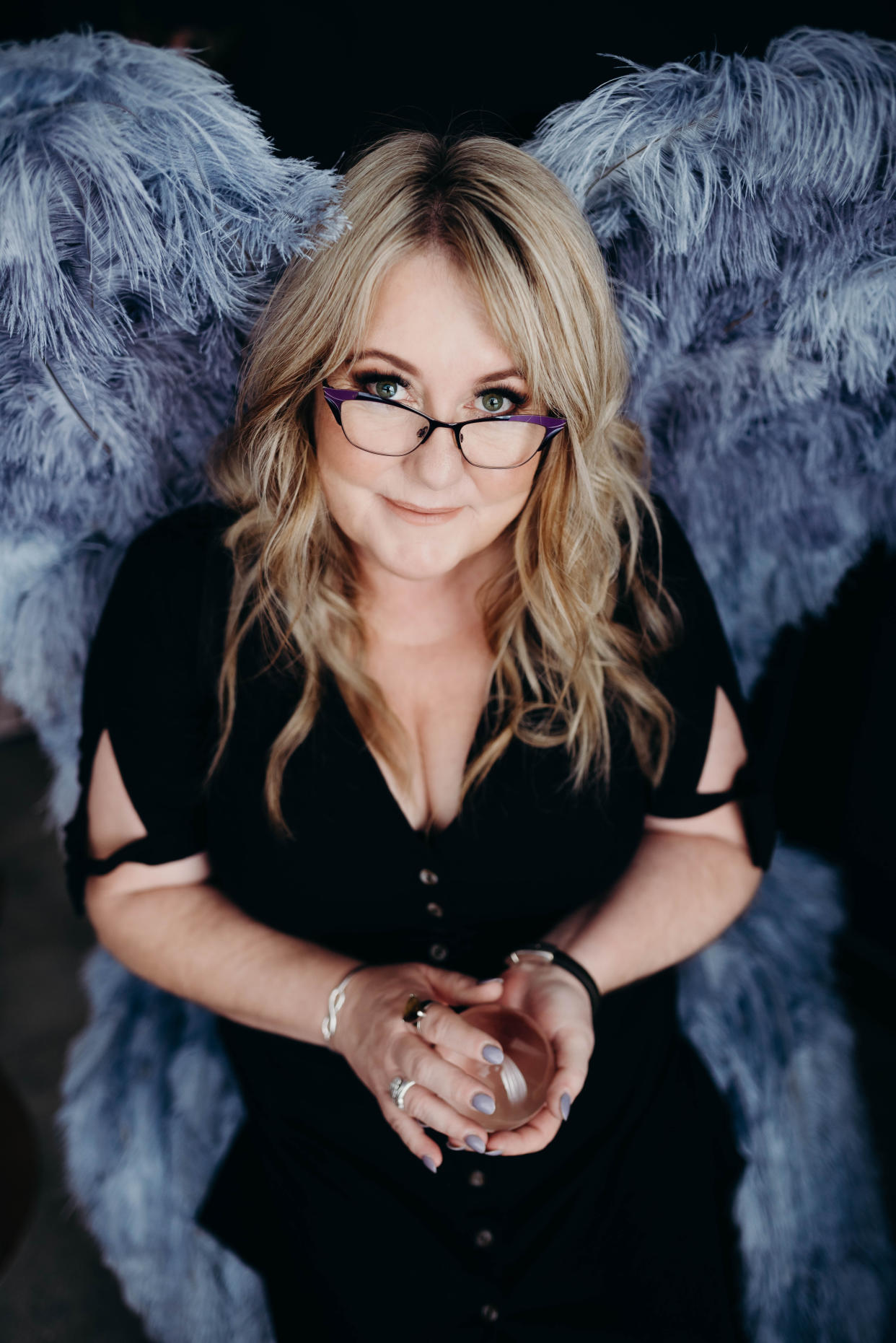 A woman wearing glasses sits on a feathered throne