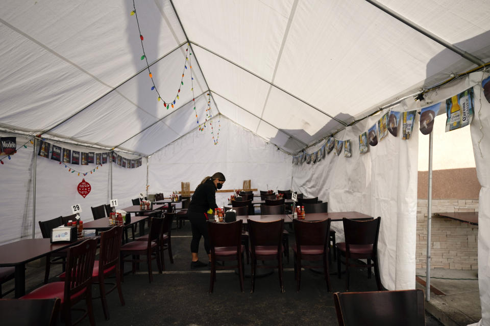 A restaurant worker cleans the tables in the outdoor dining area of a Mexican restaurant in La Mirada, Calif., Tuesday, Nov. 24, 2020. Waiters and bartenders are being thrown out of work – again – as governors and local officials shut down indoor dining and drinking establishments to combat the nationwide surge in coronavirus infections that is overwhelming hospitals and dashing hopes for a quick economic recovery. (AP Photo/Jae C. Hong)