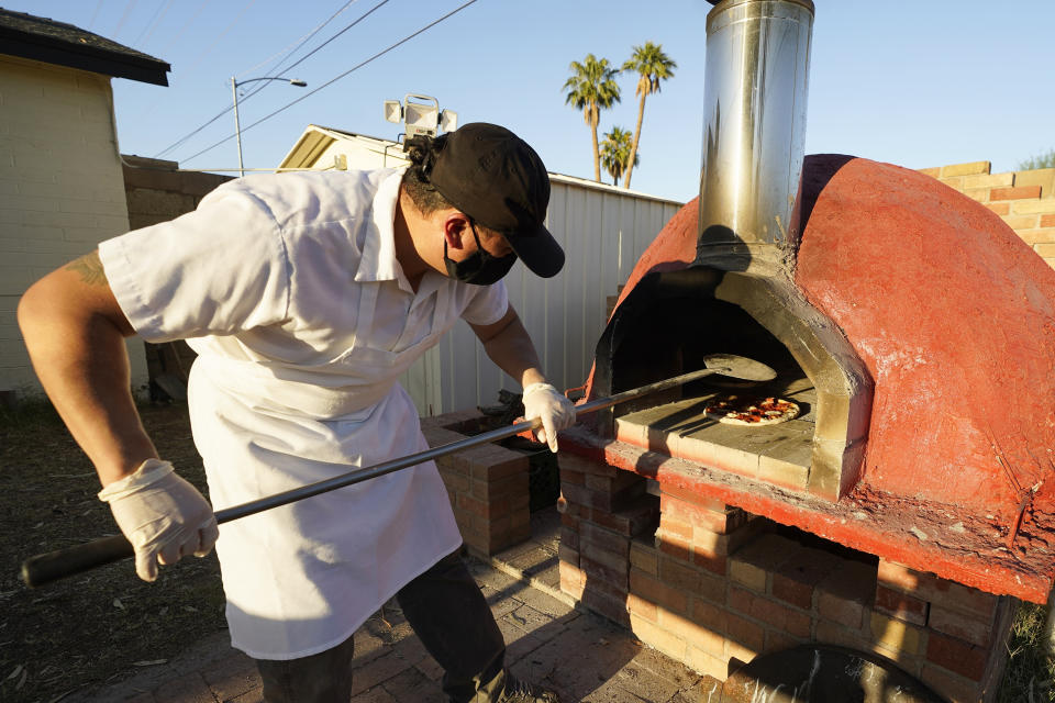 Chef Jose Hernandez checks on several pizzas in a clay oven in a makeshift backyard pizza kitchen on April 3, 2021, in Scottsdale, Ariz. Beaten down by the pandemic, some laid-off or idle restaurant workers have pivoted to dishing out food from home. (AP Photo/Ross D. Franklin)