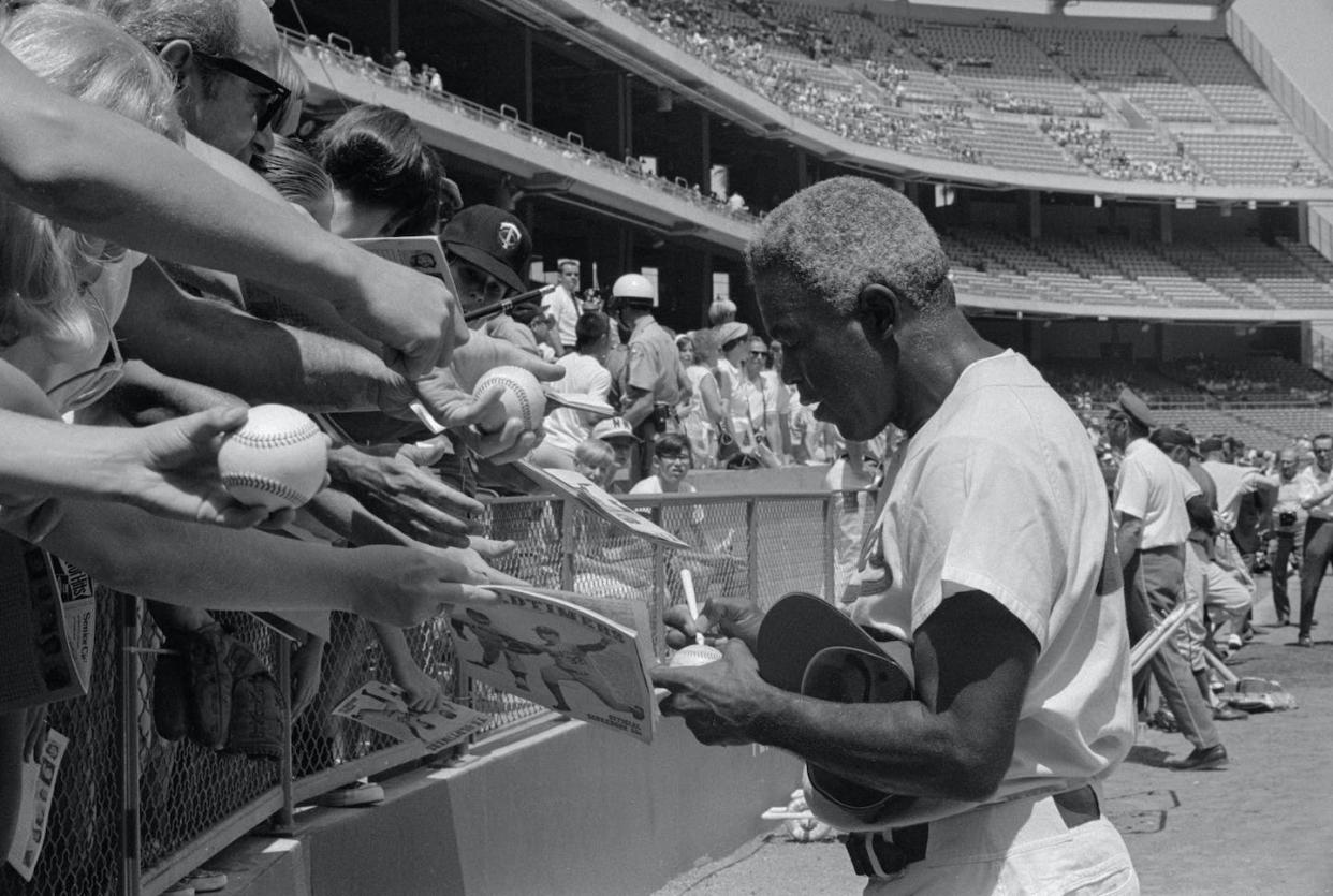 Adoring fans clamor for an autograph from baseball legend Jackie Robinson in 1962, but Robinson faced slurs, hatred and insults in his early years in the majors. <a href="https://www.gettyimages.com/detail/news-photo/former-dodger-great-jackie-robinson-signs-autographs-before-news-photo/515392368?adppopup=true" rel="nofollow noopener" target="_blank" data-ylk="slk:Bettman/;elm:context_link;itc:0;sec:content-canvas" class="link ">Bettman/</a>