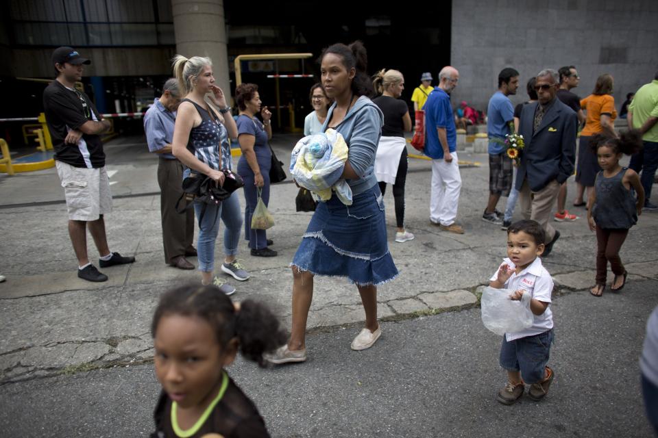 Una mujer con su bebé camina frente a una cola de gente formada para comprar alimentos en Caracas, Venezuela, sábado 18 de agosto de 2018. La oposición venezolana llama a un paro nacional para el 21 de agosto en protesta por las medidas económicas que anunció el presidente Nicolás Maduro. (AP Foto/Ariana Cubillos)