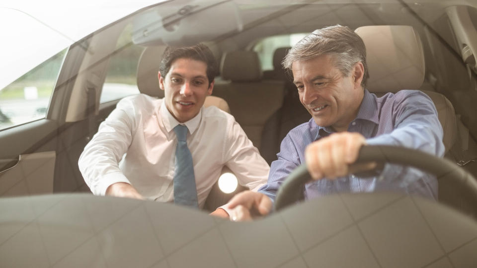 Businessman pointing a car interior at new car showroom.