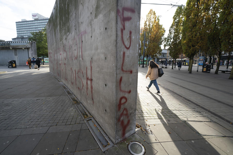 A woman walks by coronavirus related graffiti on a wall, in Manchester, England, Tuesday, Oct. 20, 2020. The British government appeared poised Tuesday to impose strict coronavirus restrictions on England's second-largest city after talks with officials in Greater Manchester failed to reach an agreement on financial support for people whose livelihoods will be hit by the new measures. (AP Photo/Jon Super)