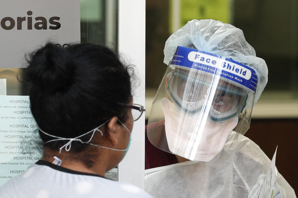 A medical worker in protective gear speaks to a woman wearing a mask at the door of the ward designated for respiratory emergencies, at Dr. Manuel Gea Gonzalez General Hospital, one of many treating patients with symptoms of the new coronavirus in Mexico City, Wednesday, April 22, 2020. Several people waiting outside for news of their hospitalized relatives said their family members were being treated in the waiting room since yesterday, since beds in the respiratory ward were full. (AP Photo/Rebecca Blackwell)