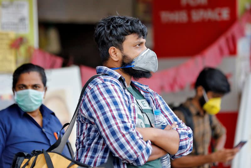 People wearing protective masks wait to board a bus at a terminal amid coronavirus fears, in Kochi