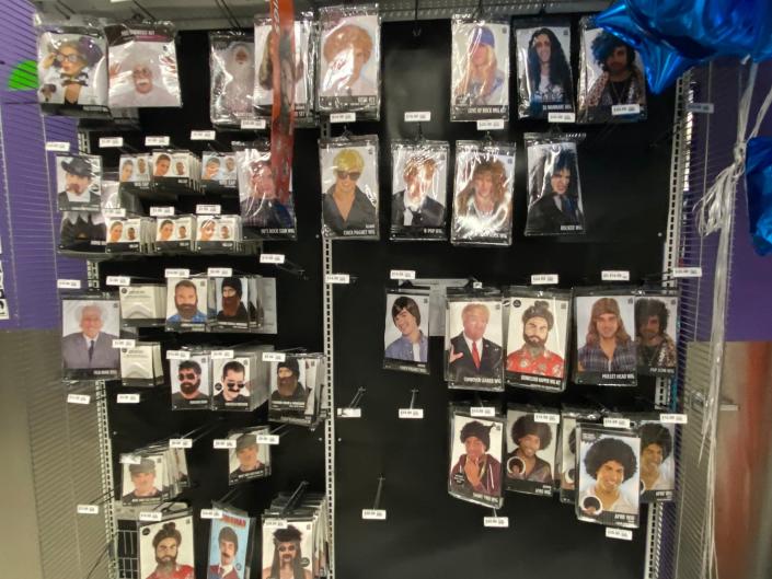 A few wigs hanging from shelving in party city