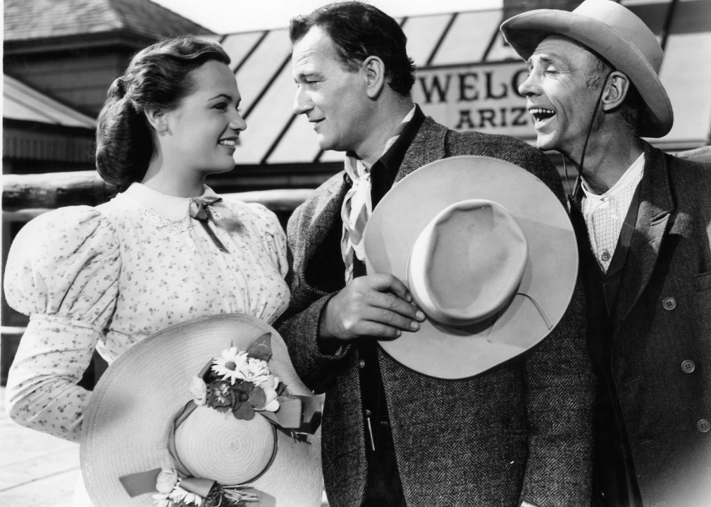 Dorothy Ford and John Wayne looking into each other's eyes as a man watches in a scene from the film '3 Godfathers' from 1948.