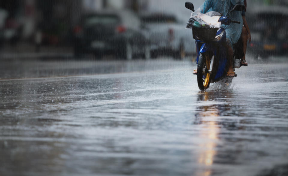 A couple with raincoat on a motorbike during hard rainfall/Dramatic scene of rainy season in Southeast Asia).Selective focus and very shallow depth of field composition.