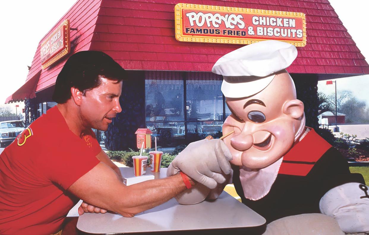 Al Copeland (left), founder of the Popeyes fried chicken chain, arm wrestles with the famous strongman Popeye.