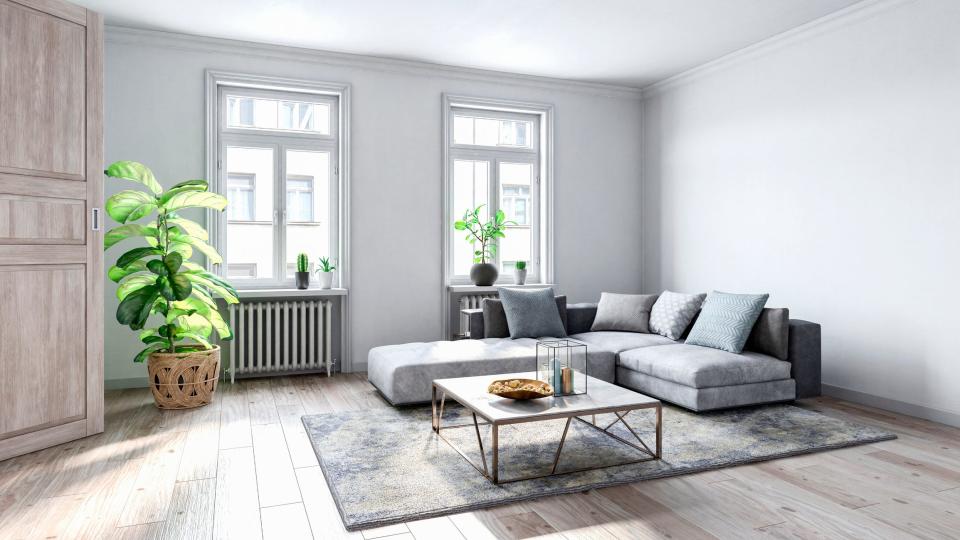 Gray sectional couch on blue rug in front of plain gray walls in minimalist living room