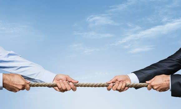 The arms of two men in business attire engaged in a tug of war.