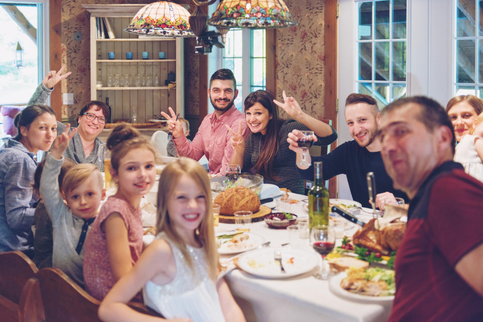 Family and friends gathered around a dinner table, smiling and making peace signs