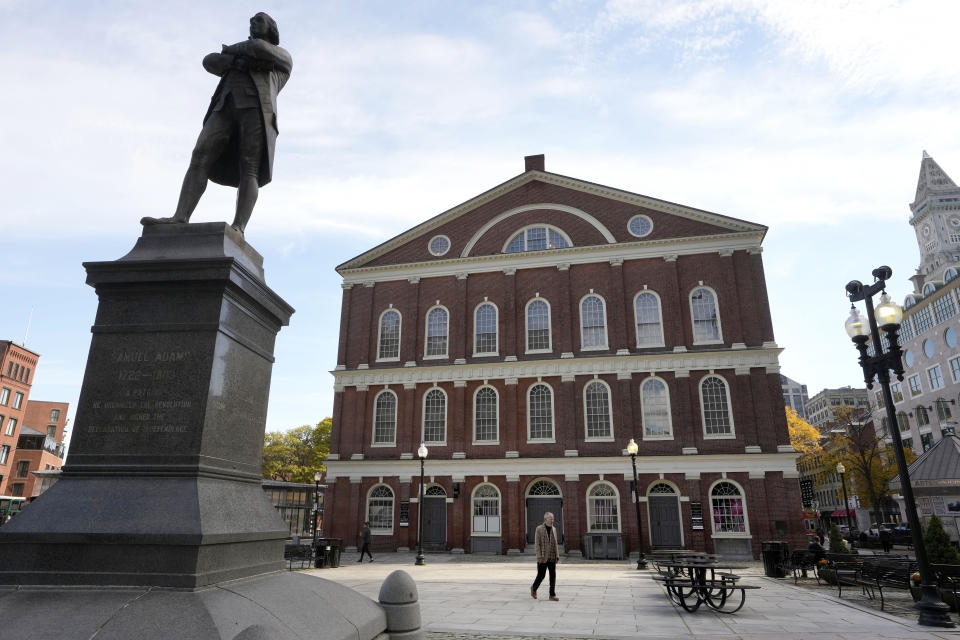 A statue of Samuel Adams, left, stands near Faneuil Hall, behind, Wednesday, Oct. 25, 2023, in Boston. Boston City Council members voted Wednesday in favor of holding a hearing on the renaming of the popular tourist site. Boston City Councilor Tania Fernandes Anderson has filed a resolution decrying the building's namesake, Peter Faneuil, as a "white supremacist, a slave trader, and a slave owner who contributed nothing recognizable to the ideal of democracy." (AP Photo/Steven Senne)