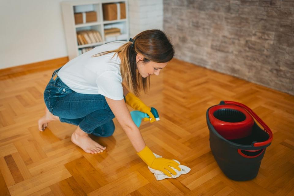 Woman using microfiber towel and bucket to clean floor.